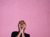 trendy young black woman touching face while throwing head back on pink background